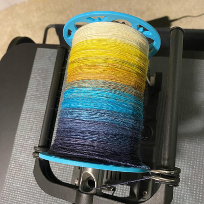 a bobbin of handspun yarn in a gradient going from dark blue to yellow