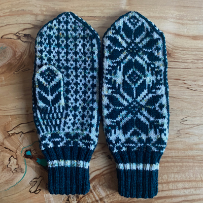 a pair of selbu mittens, one showing the back snowflake pattern and the other showing the pattern on the palm
