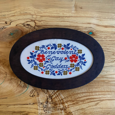 a floral cross stitch with 'benevolent gay goddess' in calligraphic text